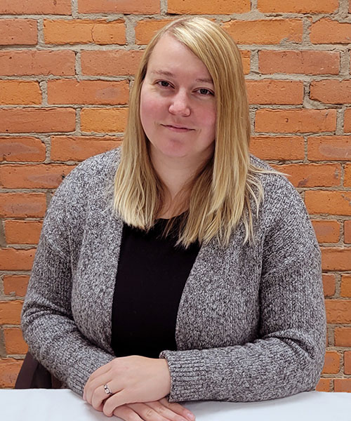 Staff headshot Ashlee Bise, in front of a brick background.