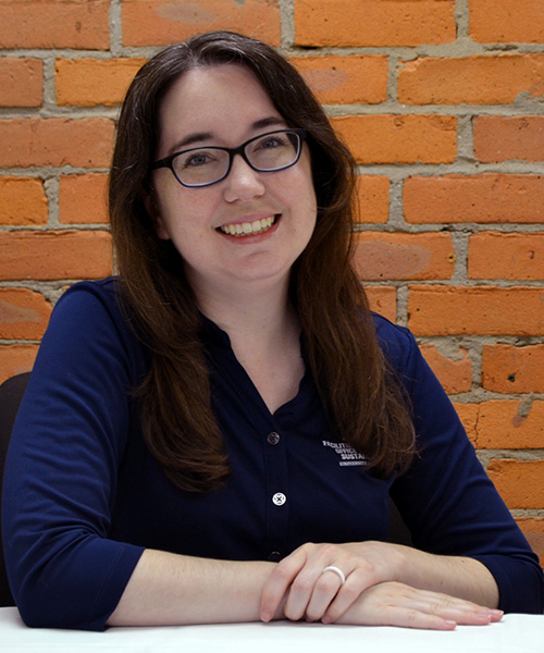 Staff headshot Nicole Berg, in front of a brick background.