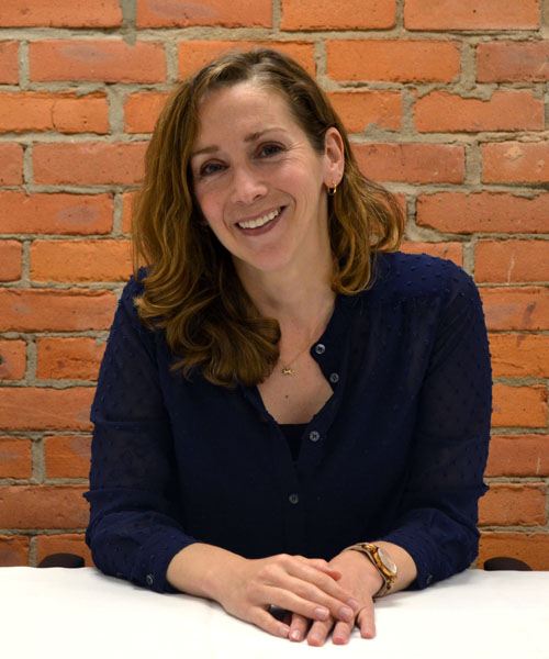 Staff headshot Anya Dale, in front of a brick background.