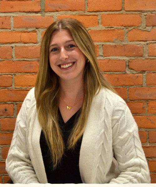 Staff headshot Alexandria Galens, in front of a brick background.